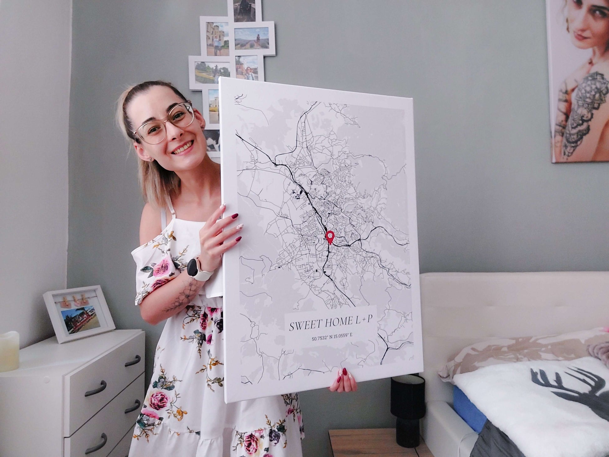 Woman smiling while holding a custom city map poster in bedroom setting.